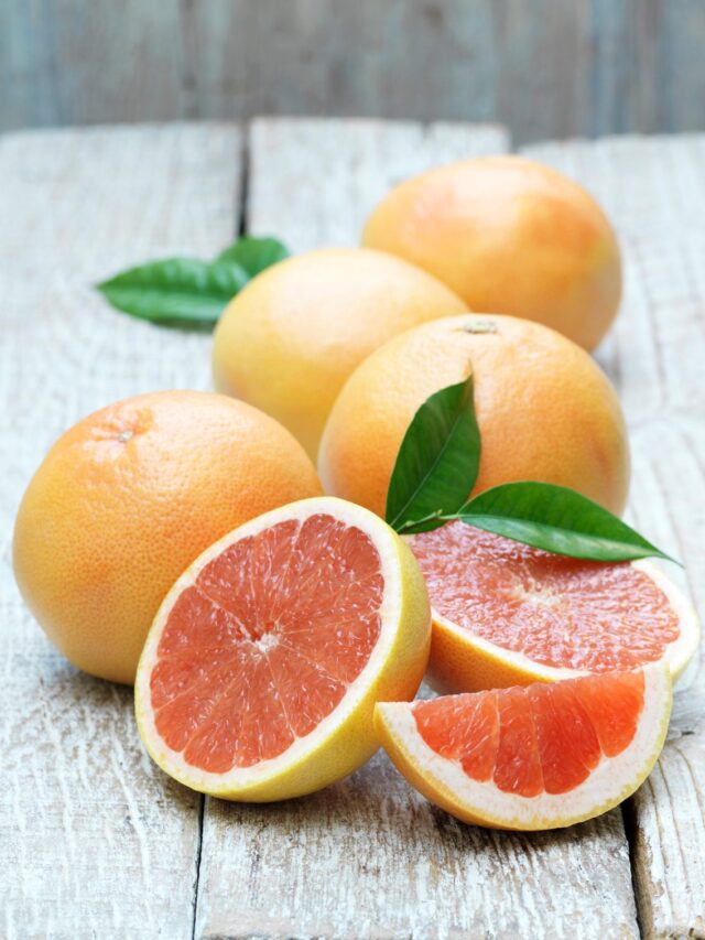 Whole and half pink grapefruit on whitewashed wooden table