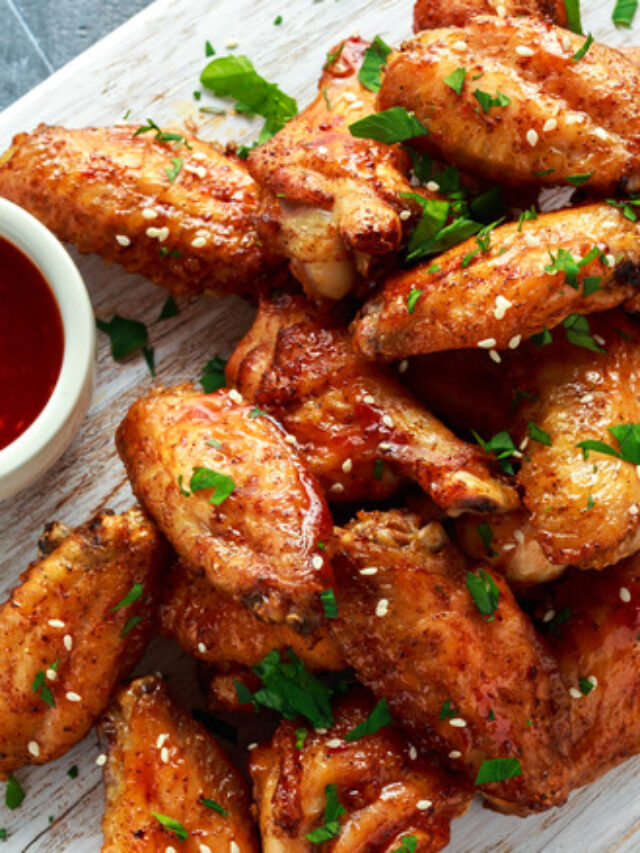 Baked chicken wings with sesame seeds and sweet chili sauce on white wooden board.